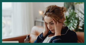 Woman experiencing physical symptoms of anxiety including stress, overwhelm, muscle tension, and difficulty concentrating while sitting at home.